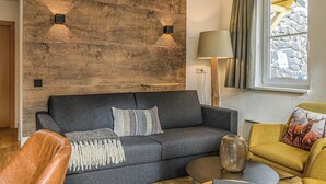 Ett modernt vardagsrum med en mörkgrå soffa, en väggpanel i trä, en lampa och ett fönster med gardiner.