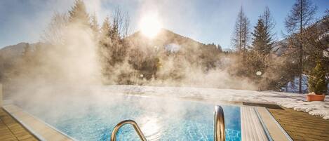 A hot spring pool with clear water, surrounded by a wooden deck and snow-covered ground.