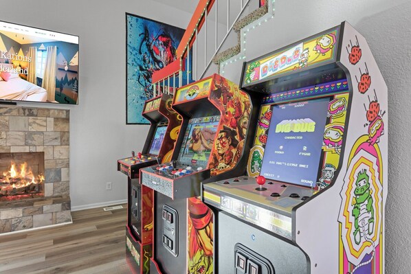 A room with arcade games, a fireplace, and a large painting on the wall.