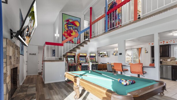 A spacious indoor area with a pool table, arcade games, and a staircase with red railings.