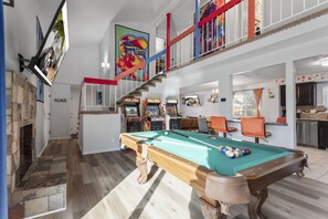 A spacious indoor area with a pool table, arcade games, and a staircase with red railings.