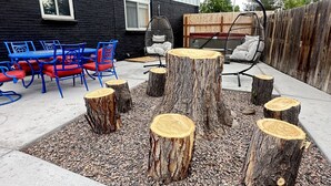 An outdoor seating area with blue and red chairs, a white sofa, and wooden stumps arranged on a gravel surface.