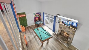 A pool table in a room with a fireplace, a painting, and a sign that reads "h Nations."