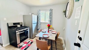 Una cocina compacta con estufa a gas, horno y refrigerador. Hay una mesa de comedor con sillas y un florero con flores.
