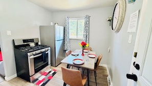 Una cocina compacta con estufa a gas, horno y refrigerador. Hay una mesa de comedor con sillas y un florero con flores.