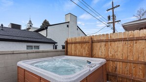 Un jacuzzi en un patio trasero con valla de madera, pared de ladrillo y una casa al fondo.