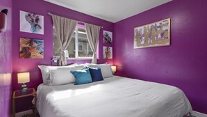 Una habitación con una cama grande, paredes moradas y obras de arte.