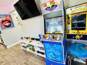 A room with arcade games, a television, and a shelf with various items. - RedRocks Cozy Unit HotTub Arcade DancePole (Wheat Ridge)