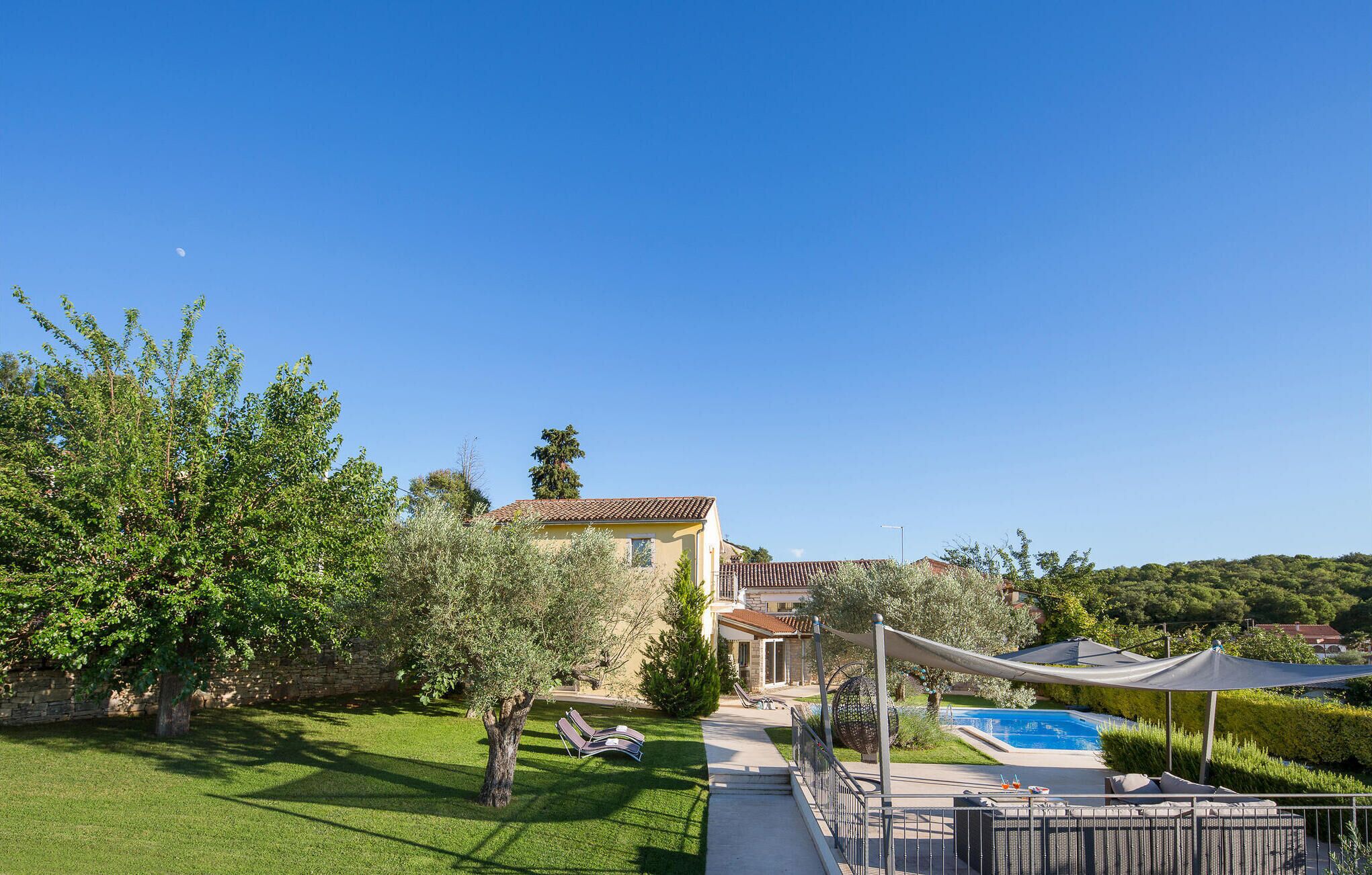Une maison avec une piscine, un jardin et un ciel bleu azur.
