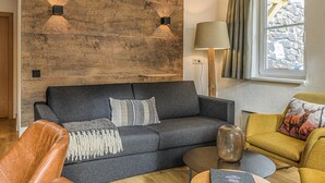 Un salon moderne avec un canapé gris foncé, un mur d’accent en bois, une lampe et une fenêtre avec des rideaux.
