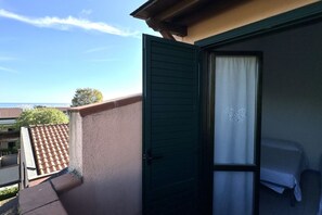 A balcony with a tiled roof, a green door, and a bed with a white sheet.