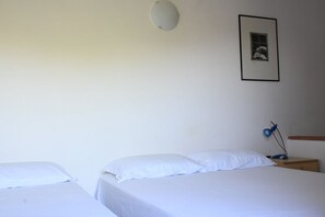 A bedroom with two beds, a nightstand with a lamp, a framed picture on the wall, and a ceiling light.