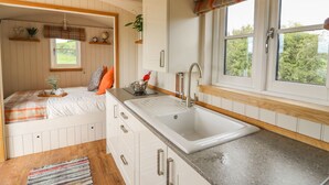 A compact kitchen with a sink, wooden countertop, and a window with a plaid valance.