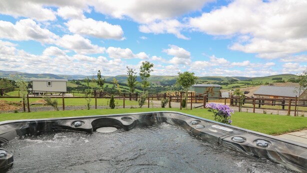 A hot tub with a scenic view of a countryside landscape, including green fields and a wooden fence. - Hillside View Shepherds Hut Sleeps 2 (Rhayader)
