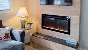 A modern living room with a flat-screen TV mounted above a fireplace, a lamp, and a welcome sign. - Cozy cottage with amazing view on the Big Bald Lake in Bobcaygeon (Bobcaygeon)