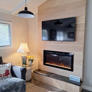 A modern living room with a flat-screen TV mounted above a fireplace, a lamp, and a welcome sign.