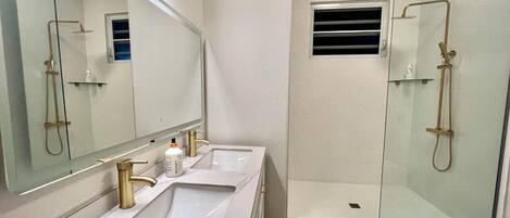 Un baño moderno con dos lavamanos, un espejo grande y una ducha con mampara de vidrio.
