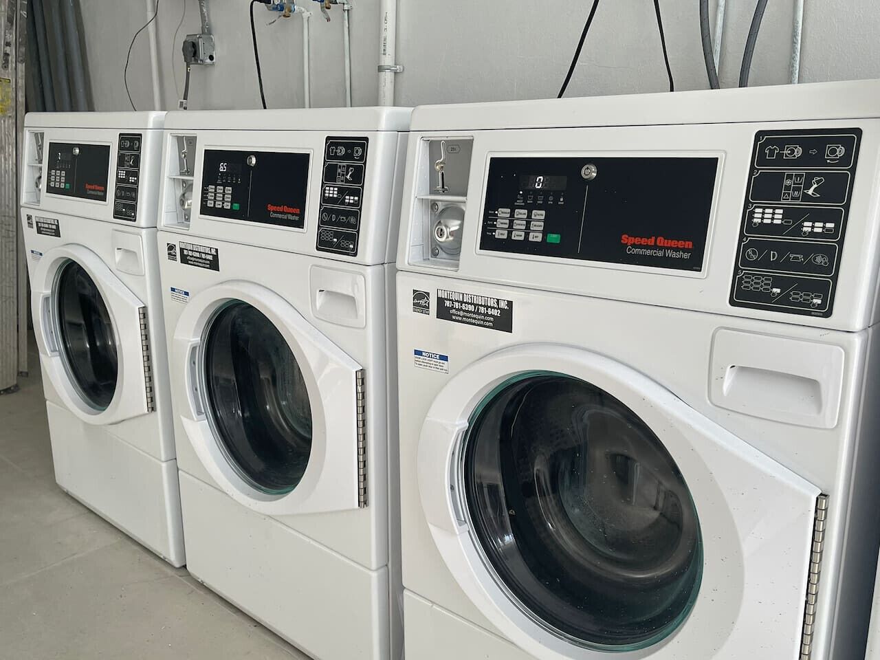 A row of white commercial washers with control panels, labeled "Speed Queen Commercial Washer."