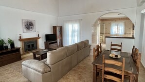 Een ruime woonkamer met een grote bank, eettafel en een open haard.