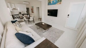 Una sala de estar moderna con un sofá blanco, una mesa de centro y un televisor de pantalla plana montado en la pared.