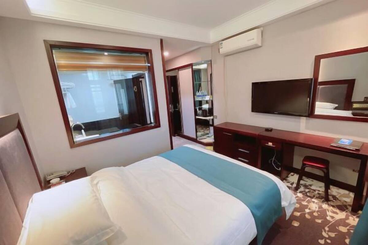 Ein Hotelzimmer mit Bett, Schreibtisch, Stuhl, Fernseher und einem großen Fenster.
