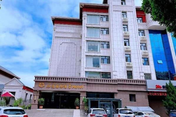 Un hôtel à plusieurs étages, doté d’une entrée imposante, d’un espace de stationnement à l’avant et d’un bâtiment moderne attenant.