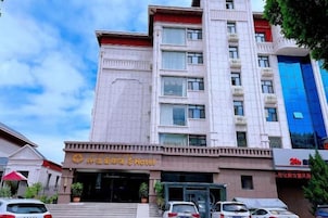 Un hotel de varios pisos con una entrada destacada, un estacionamiento frente al edificio y una construcción moderna contigua.