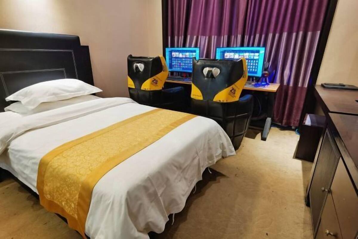 Ein Hotelzimmer mit einem Bett, zwei Bildschirmen und einem Schreibtisch mit zwei Stühlen.