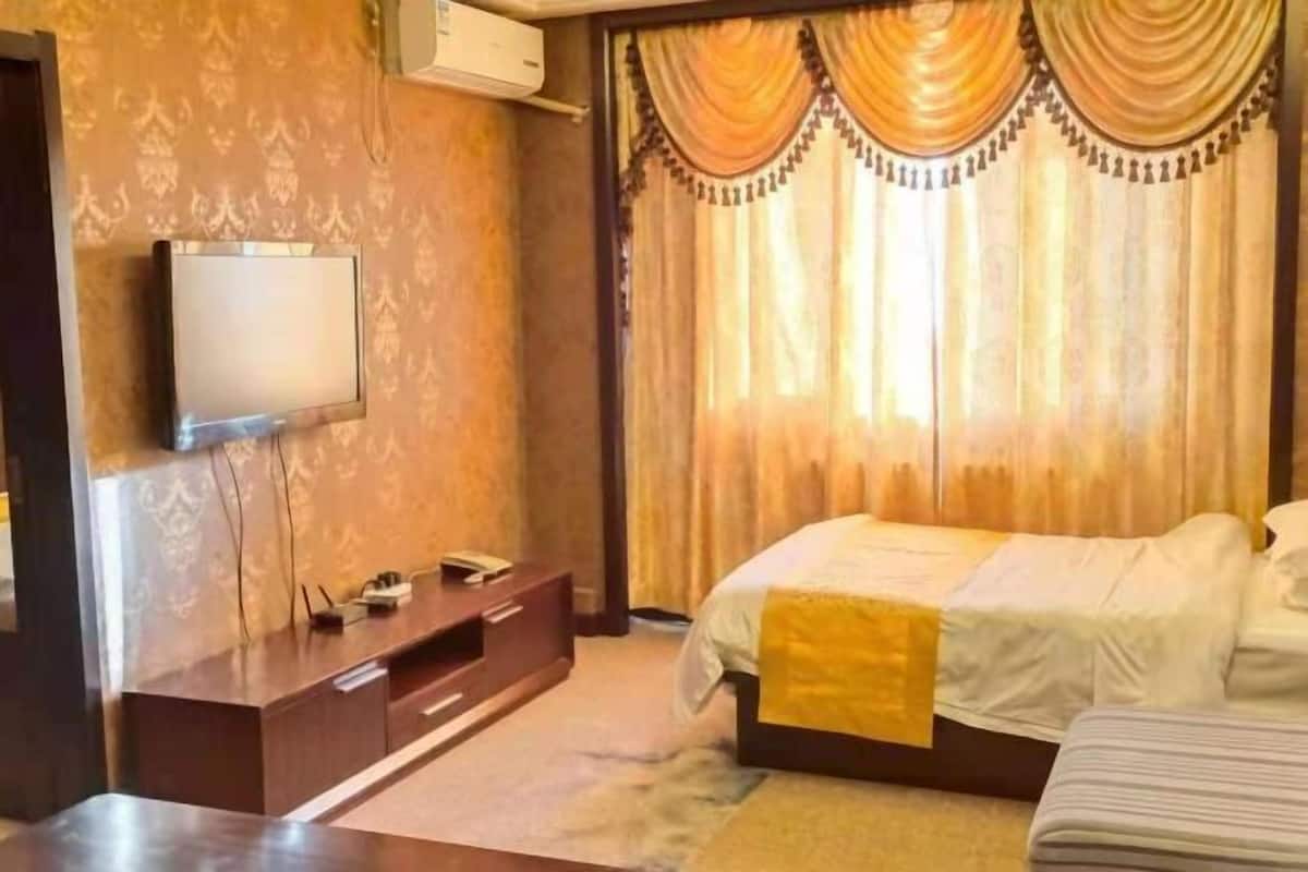 Ein Hotelzimmer mit einem Bett, einem an der Wand montierten Fernseher, einer hölzernen Kommode und einem Fenster mit Vorhängen.