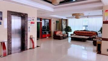 A hotel lobby with a reception desk, a seating area with a sofa and armchairs, and a large chandelier.