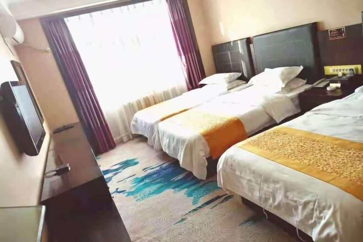 Ein Hotelzimmer mit zwei Betten, einem Flachbildfernseher, einem Schreibtisch und einem Vorhangfenster.