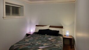 Een slaapkamer met een bed, twee nachtkastjes, een venster met zonwering en een plafondlamp.
