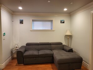 A living room with a sectional sofa, a small side table, a floor lamp, and a window with blinds.
