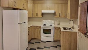 Een kleine keuken met houten kastjes, een witte koelkast, een fornuis en een spoelbak.
