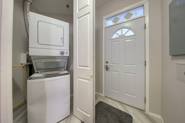 A laundry room with a front-loading washer and dryer, a door with a decorative glass panel, and a gray rug on the floor.