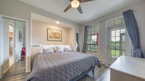 Ein Schlafzimmer mit einem großen Bett, einem Deckenventilator, einem Gemälde an der Wand und Blick durch das Fenster.