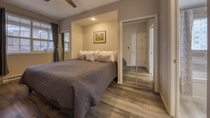Una camera da letto con un letto grande, una ventola a soffitto, una finestra con tende, una porta che dà su un armadio e un quadro appeso al muro.