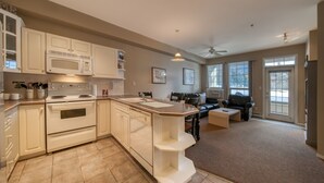 A spacious kitchen with a central island, a dining area with a sofa, and a view of the outdoors through large windows. - Mountain Rook 2 king bedroom, sleeps 6: Unit 1002 (Fairmont Hot Springs)