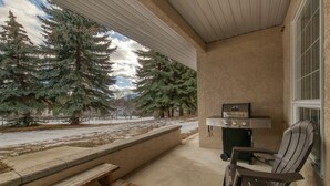 A covered patio with a grill, a wooden bench, and a chair. - Mountain Rook 2 king bedroom, sleeps 6: Unit 1002 (Fairmont Hot Springs)