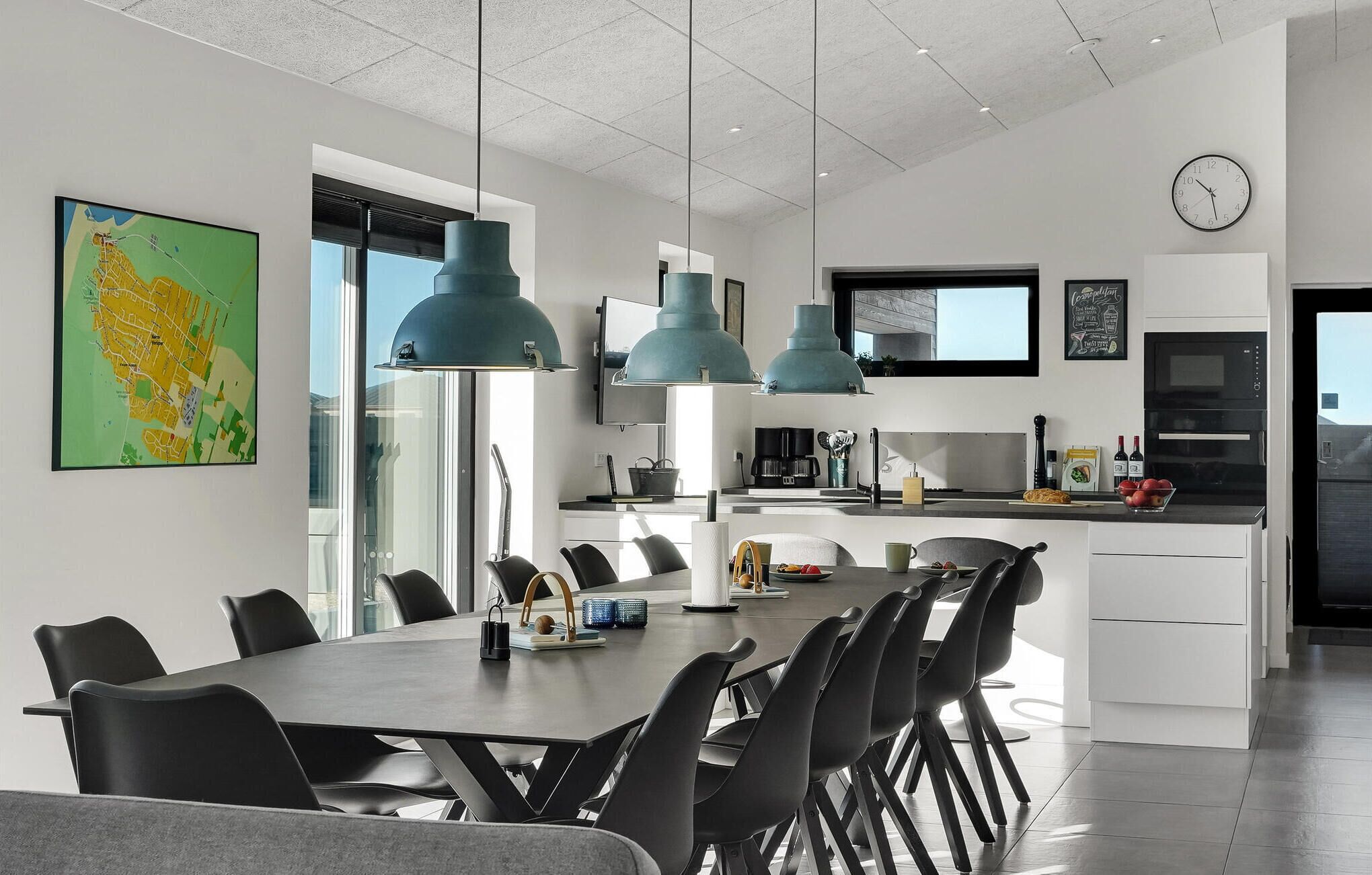 Cozinha moderna com ilha central, luminárias pendentes e área de jantar com mesa grande e cadeiras.
