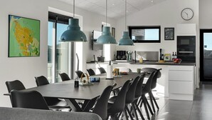 A modern kitchen with a central island, pendant lights, and a dining area with a large table and chairs.