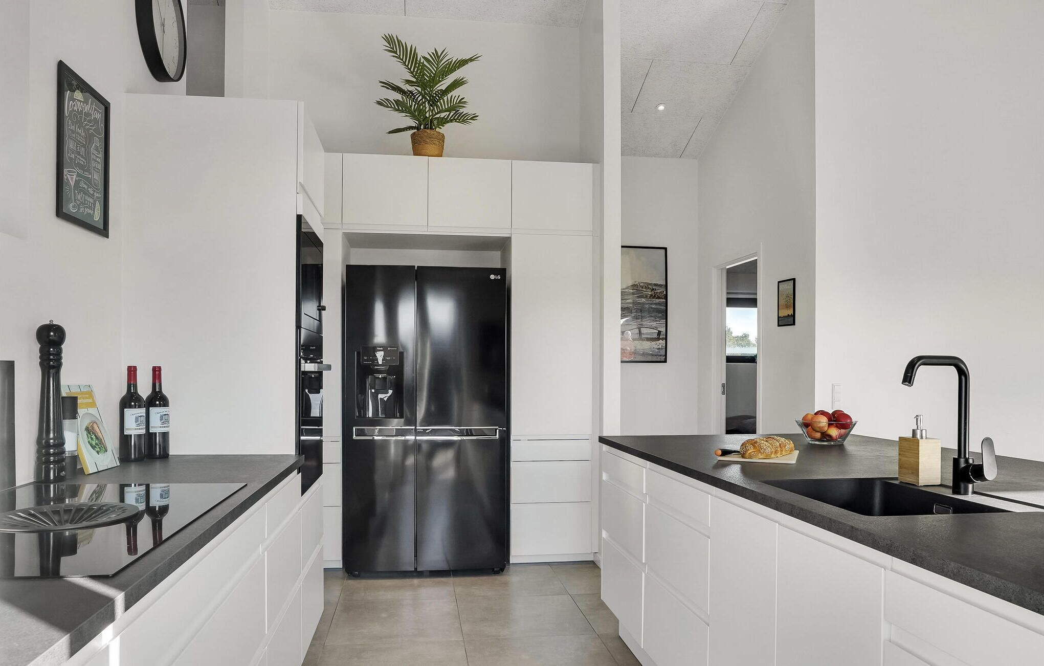 Een moderne keuken met witte kasten, een roestvrijstalen koelkast, een zwart aanrecht en een potplant.