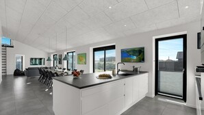 A modern kitchen with a large island, a dining area with a long table, and a view of a cityscape through large windows.