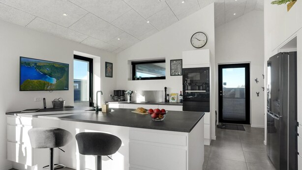 A modern kitchen with a large island, bar stools, a clock, and a refrigerator.