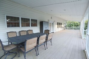 A covered porch with a dining table and chairs, a clock, and a white railing.
