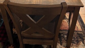 A wooden dining table with four chairs, a water dispenser, and a small glass with a straw.