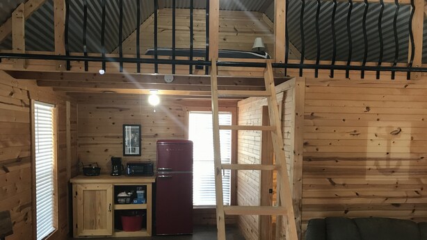 Interior de una cabaña de madera con cocina, una mesa de comedor y un sofá.