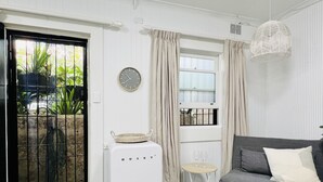 A compact living space with a grey sofa, a white radiator, a wall clock, and a window with curtains. - Live like a local in the heart of Surry Hills (Surry Hills)