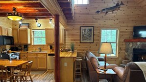 Un acogedor interior de cabaña con comedor de madera, cocina y sala de estar con sofá y chimenea.