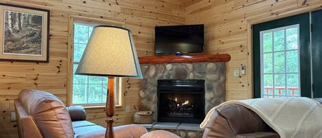 L’intérieur chaleureux d’un chalet avec des murs en bois, une cheminée en pierre, des sièges en cuir et un poisson empaillé accroché au mur.